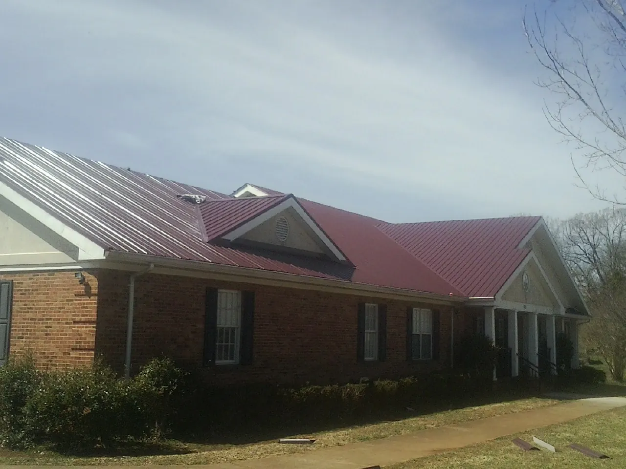 Red metal roof with gabled entries on a long brick building, from a Hail Damage Roof Repair job in Lewiston